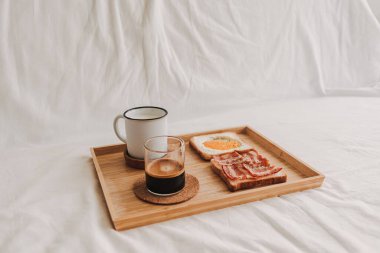 Easy and simple breakfast set of Bacon Sandwich served with black coffee on bed.