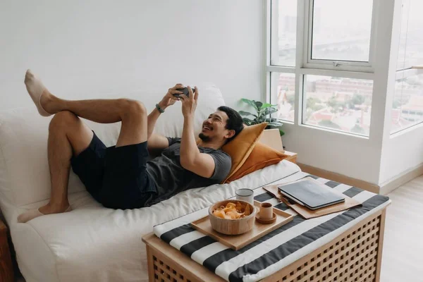 Lazy happy asian man playing mobile game while he should have work from home.