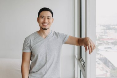 Ordinary happy life smile face asian man stand by the window in his apartment.