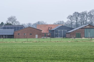 Ahırlar ve ahırlar kısmen kırmızı çatılı bir çiftlik evinin yakınındaki güneş panelleriyle.