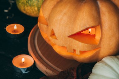 Cadılar Bayramı Balkabağı, Jack O Lantern. Balkabağı manzaralı. Yakınlarda bir çift mum var, biri kafasının içinde yanıyor. Balkabağı tahtanın üzerinde..