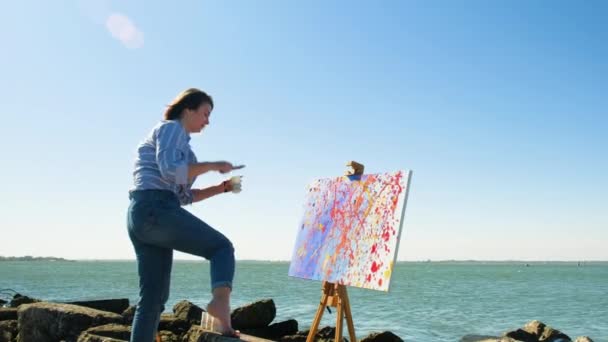 Talentierte Künstlerin streut mit Pinsel Farbe auf Leinwand am Flussufer. — Stockvideo