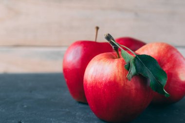 Gri bir masanın üzerine yakın plan birkaç elma, arka plan tahtasına karşı. Boşluğu kopyala