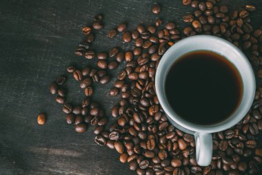 Beyaz bir fincan kahve koyu ahşap bir arka planda kahve çekirdekleri ile çevrilidir. Uzayı kopyala Yukarıdan bak. Sade kahve