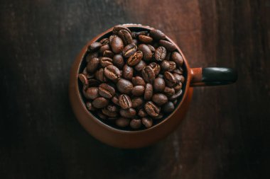 Ahşap masada kavrulmuş kahve çekirdekleri ile dolu killi kahve fincanının yakın çekim görüntüsü.