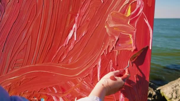 Mano de una artista femenina de cerca dibujando un cuadro sobre lienzo con una espátula. — Vídeos de Stock