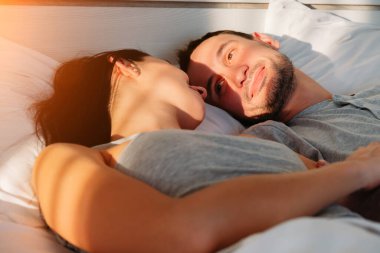 Genç evli çift sabah yatak odasında uyanıp birbirlerine bakıyorlar. Adam genç karısına sevgi dolu bir bakışla bakıyor. Mutlu aile günaydın konsepti.