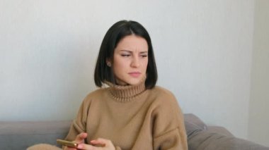 Evdeki kanepede oturan beyaz görünümlü tatlı genç kız cep telefonu kullanıyor. Bir fikir ya da çözüm arayan kız, başarılı bir seçimden memnun, basmaya devam ediyor.