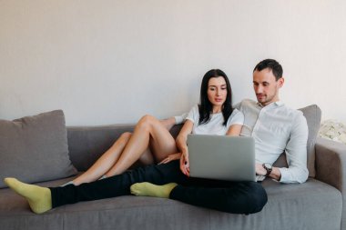 Kanepede yan yana oturan genç adam ve kadın internette alışveriş yapmak, sohbet etmek, haber veya posta izlemek için dizüstü bilgisayar kullanıyorlar. Her gün aile hayatı.
