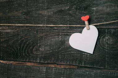 Kartondan yapılmış boş beyaz bir kalp, dekoratif bir mandalla ipte asılı duruyor. Sevdiğin için hatırlat.