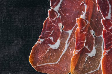 Jamon Cured Meat is laid out on wooden black kitchen board. Gluten free product. Copy space