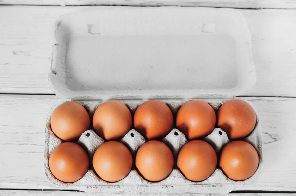 Top view of an open cardboard container with chicken eggs which lies on white table. Copy space.