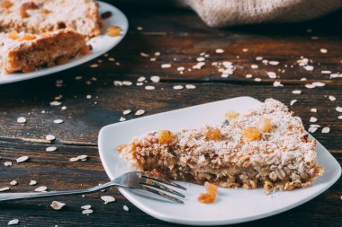 Beyaz tabakta bir parça elmalı yulaflı turta. Kuru üzümlü şekersiz lezzetli sağlıklı hamur işi..