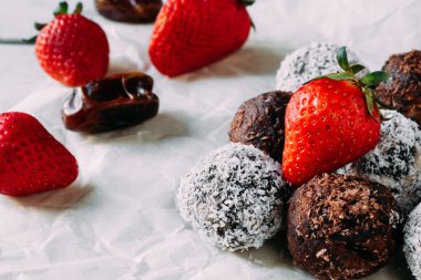 Üzerinde hindistan cevizi ve çikolata parçacıkları olan çikolatalı kek topları. Masanın üzerinde çilekli çikolatalı brownie..