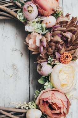 Hasır çelengin bir parçası, yakın plan yumurta ve çiçeklerle birlikte. Tahta beyaz bir kapıda asılı Paskalya çelengi