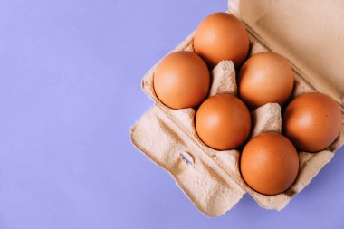 Mor arka planda kahverengi yumurtaları olan açık bir karton kutunun üst görüntüsü. Çok amaçlı popüler bir gıda ürünü..