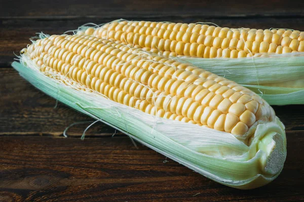 Couple of heads of unpeeled corn on table. Harvest of sweet corn.