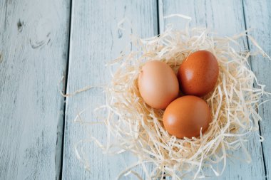 Several brown chicken eggs on straw on wooden background. Copy space.