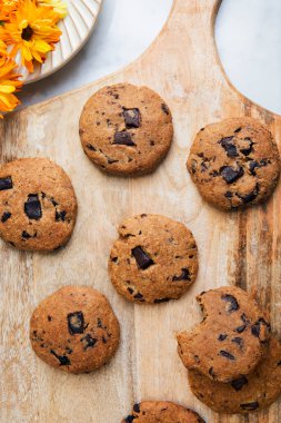 Tahta kesim tahtasında çikolatalı kurabiyelerin ve turuncu çiçeklerin üst görüntüsü.