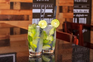 Limon dilimi ve biberiye filizi serpiştirilmiş bar arka planıyla süslenmiş buzlu, soğuk modern gurme cin ve tonik karışımı.