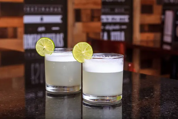 Limon dilimi ve biberiye filizi serpiştirilmiş bar arka planıyla süslenmiş buzlu, soğuk modern gurme cin ve tonik karışımı.