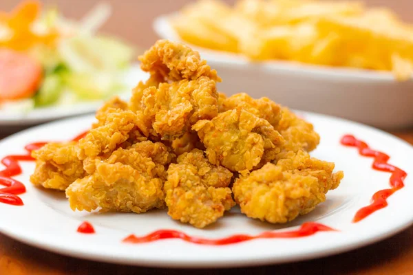 Chicken chicharron, accompanied by French fries and salad on a wooden table.