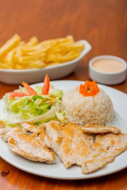 Grilled chicken accompanied by rice with french fries and salad.