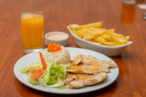 Grilled chicken accompanied by rice with french fries and salad.