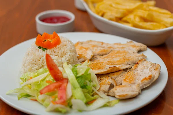 Grilled chicken accompanied by rice with french fries and salad.