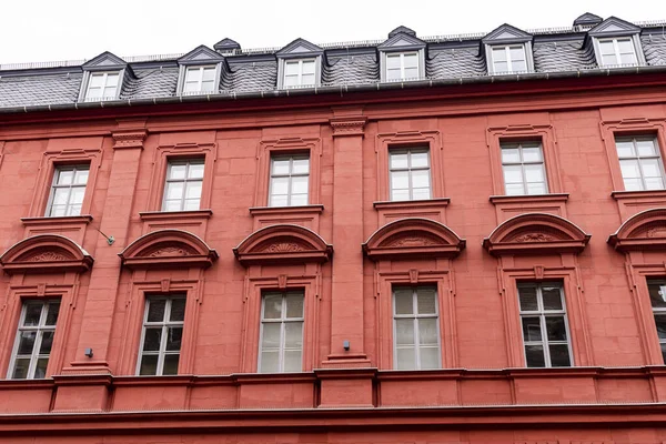 Parlak siyah kiremitleri, tavan arası pencereleri (yatakhaneler), geometrik süslemeleri ve üçgen süslemeleri olan çok sayıda penceresi olan canlı kırmızı taş apartman veya apartman dairesi.