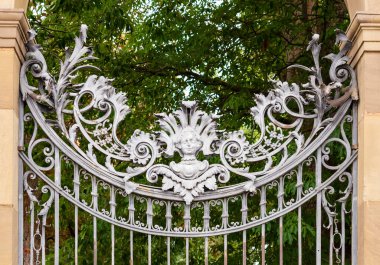 The silver ornamental gate with foliage decor and angels head, made out of metal, entrance to the Court Garden of Bavarian Residence in Wrzburg clipart