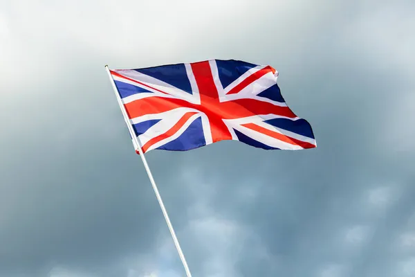 Grã-Bretanha bandeira da Inglaterra acenando ao vento sobre céu cinza nublado — Fotografia de Stock