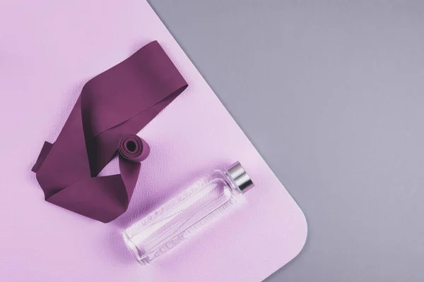 粉色瑜伽垫上的栗色膨胀机弹性带 生态可重复使用玻璃瓶的顶部视图 背景为中性灰色 — 图库照片