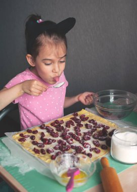 Little cute toddler girl having fun while baking or cooking in the kitchen.