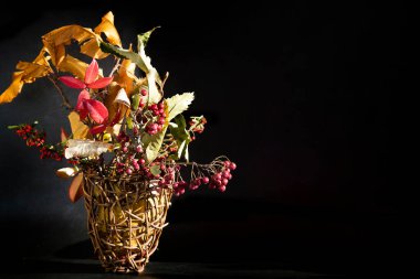 Sonbahar ikebani. Sarı kestane yaprakları, sepetin içinde kırmızı ve turuncu meyveli dallar.