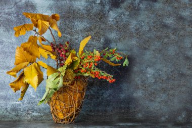 Sonbahar ikebani. Sarı kestane yaprakları, sepetin içinde kırmızı ve turuncu meyveli dallar.