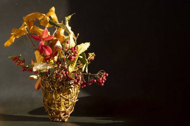 Sonbahar ikebani. Sarı kestane yaprakları, sepetin içinde kırmızı ve turuncu meyveli dallar.