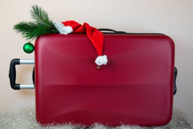 Noel tatillerinde seyahat kavramı, Noel şapkasıyla süslenmiş kırmızı bavul.