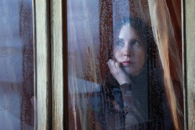 Sıkıcı kadın yağmur yağarken pencereden dışarı bakar.