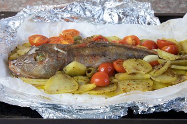 Patates, vişneli domates ve zeytinli folyoda pişmiş gurnard. Akdeniz mutfağı