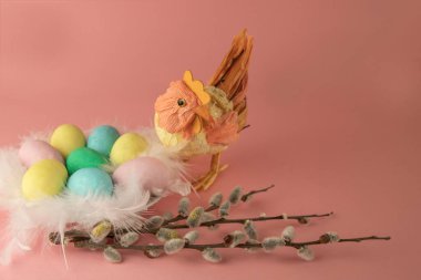  Toy handmade hen  with a nest of colored eggs decorated with pussy willow on a pink background 