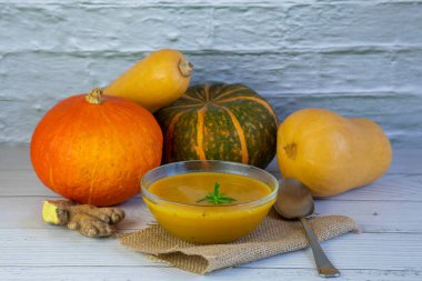 Farklı tipte balkabağı ve zencefil ile çevrili cam bir kasede ahşap bir masada kabak çorbası.