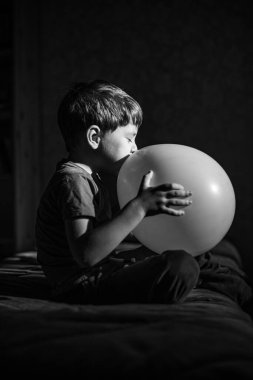 5 yaşındaki bir çocuk evinde kanepede oturuyor ve bir balonla oynuyor.