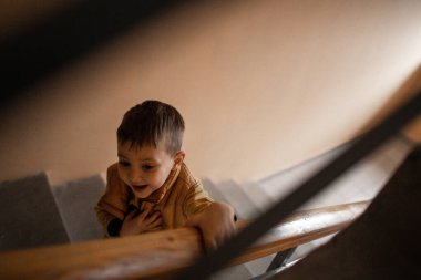 Sarı ceketli beş yaşında bir çocuk merdivenlerden girişe iniyor.