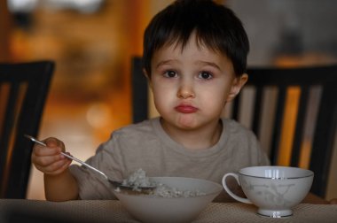 Mutfakta kahvaltı yapan, lapa yiyen ve süt içen küçük bir çocuk.
