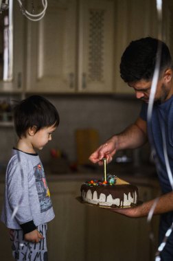 Üç yaşındaki bir çocuk doğum gününü kutluyor. Doğum günü pastasındaki mumları üflüyor.