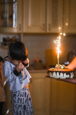 Üç yaşındaki bir çocuk doğum gününü kutluyor. Doğum günü pastasındaki mumları üflüyor.