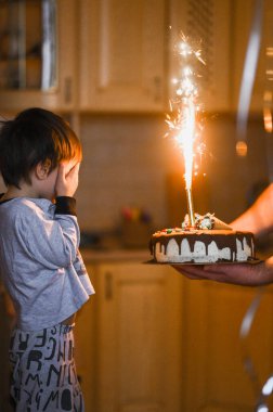 Üç yaşındaki bir çocuk doğum gününü kutluyor. Doğum günü pastasındaki mumları üflüyor.