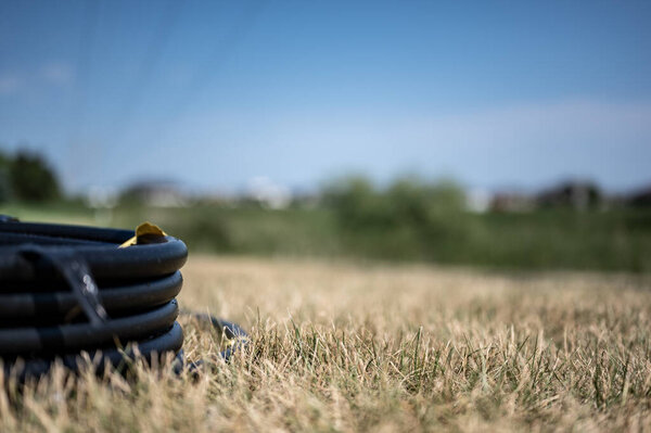 Coil of 1 inch irrigation tubing ready for new installation on top of brown and damaged dry grass.