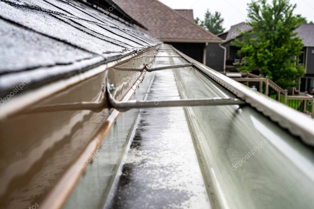 Selective focus on a section of residential guttering with hanger conveying water during a storm. Rain splatters and drops visible.